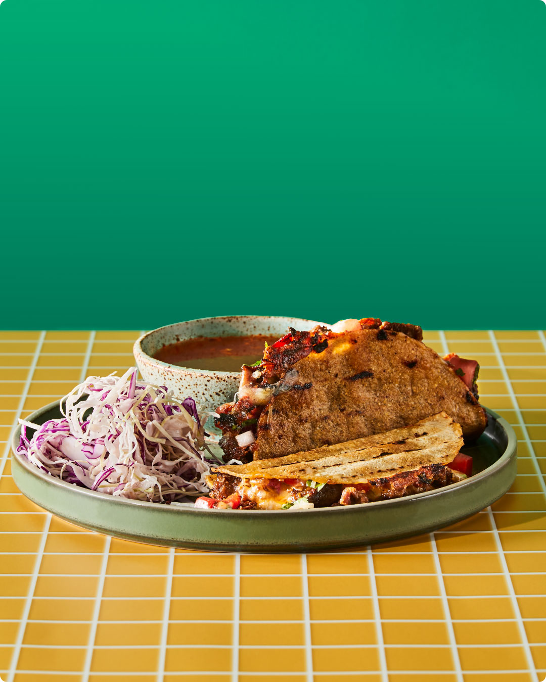 A plated Salsas birria taco with red cabbage slaw and consommé